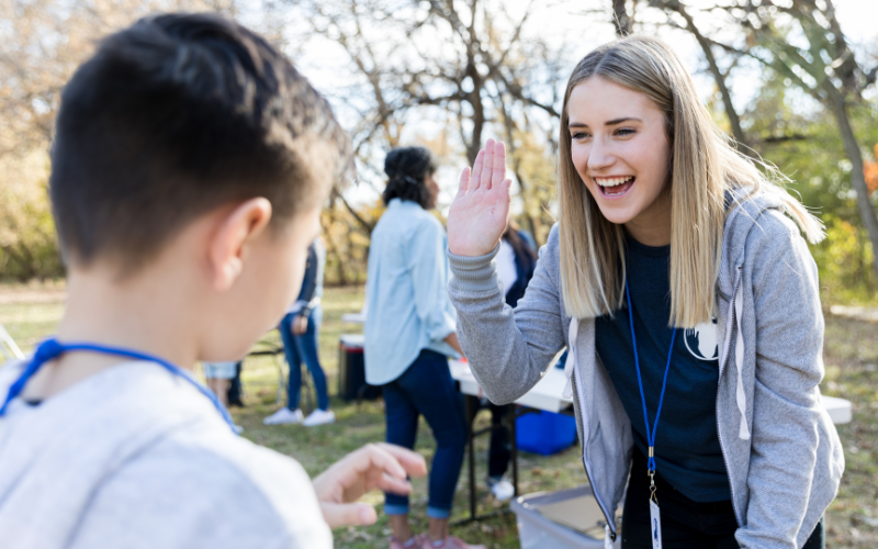 Iloinen vapaaehtoinen antaa yläfemmaa lapselle ulkona yhteisötapahtumassa.