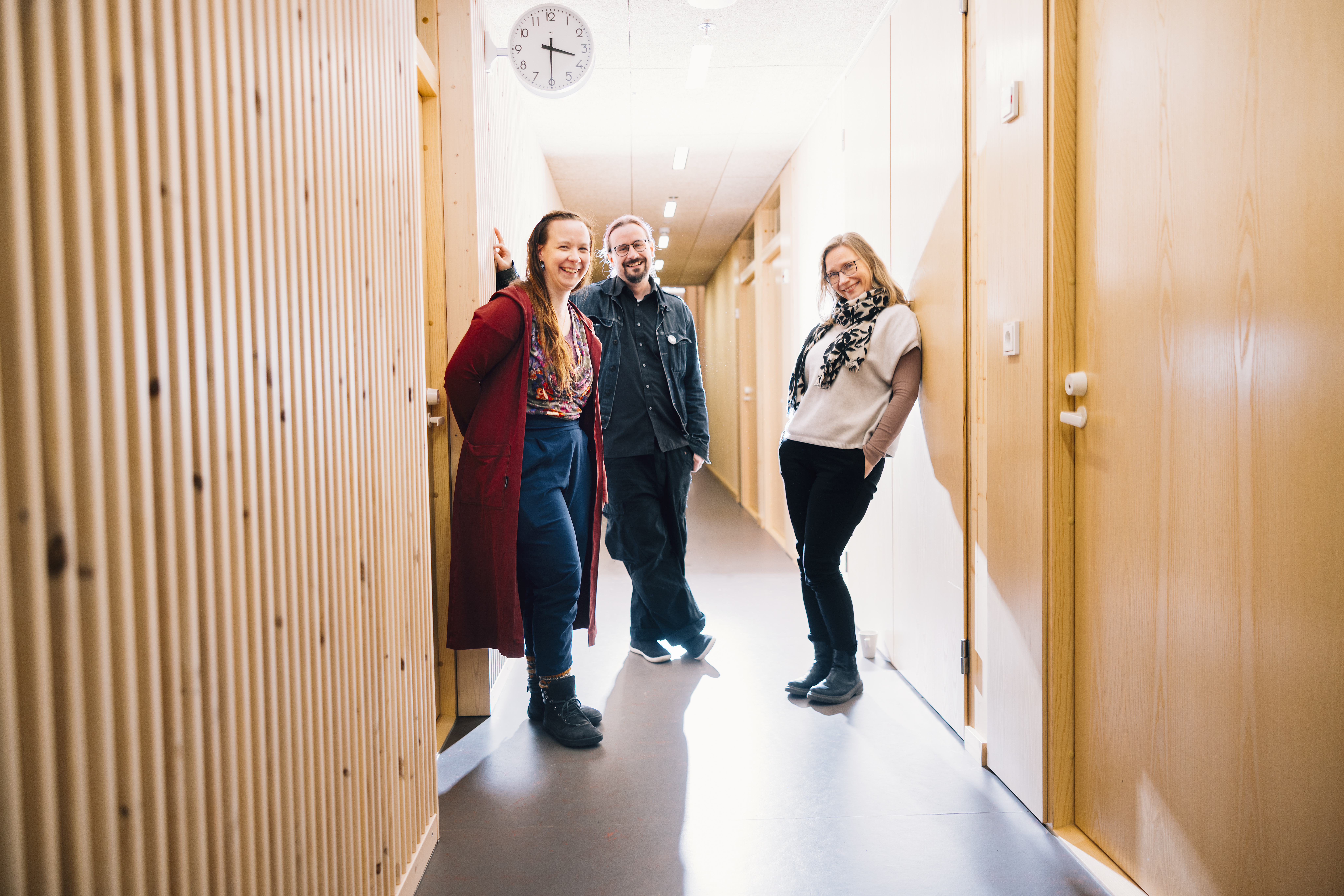Kolme henkilöä seisovat käytävällä rennosti hymyillen.