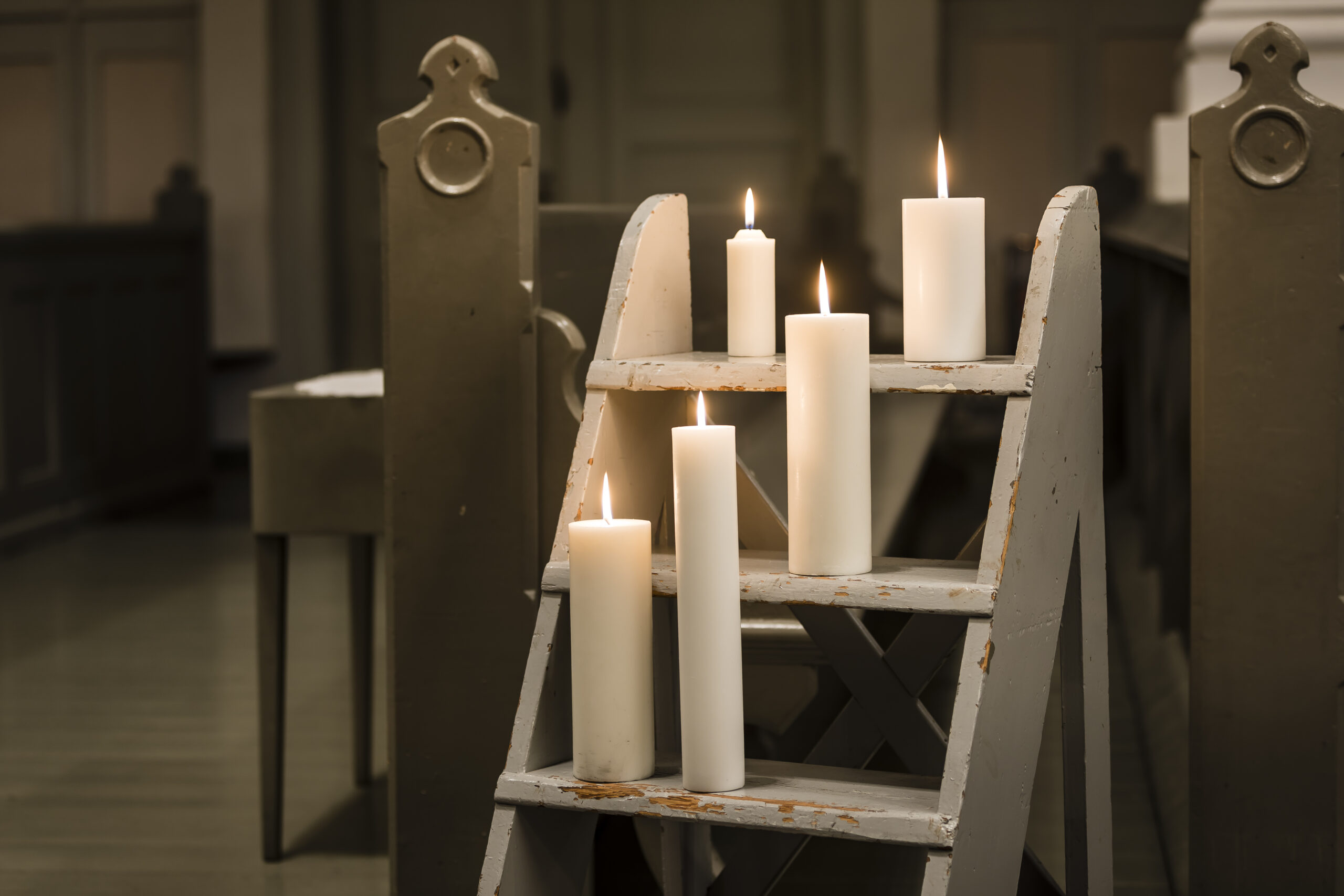 Viisi korkeaa valkoista kynttilää vanhojen tikkaiden askelmilla.