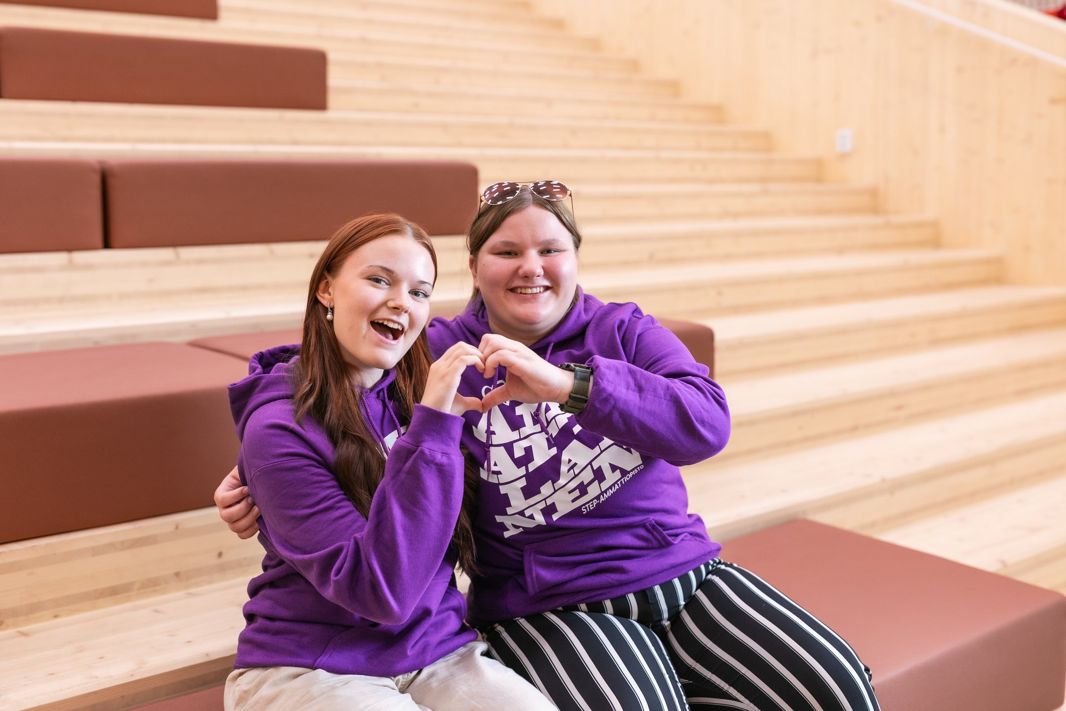 Kaksi iloista nuorta muodostaa käsistään sydämen. Molemmilla on yllä STEP-ammattiopiston paidat, joissa lukee "ammattilainen".